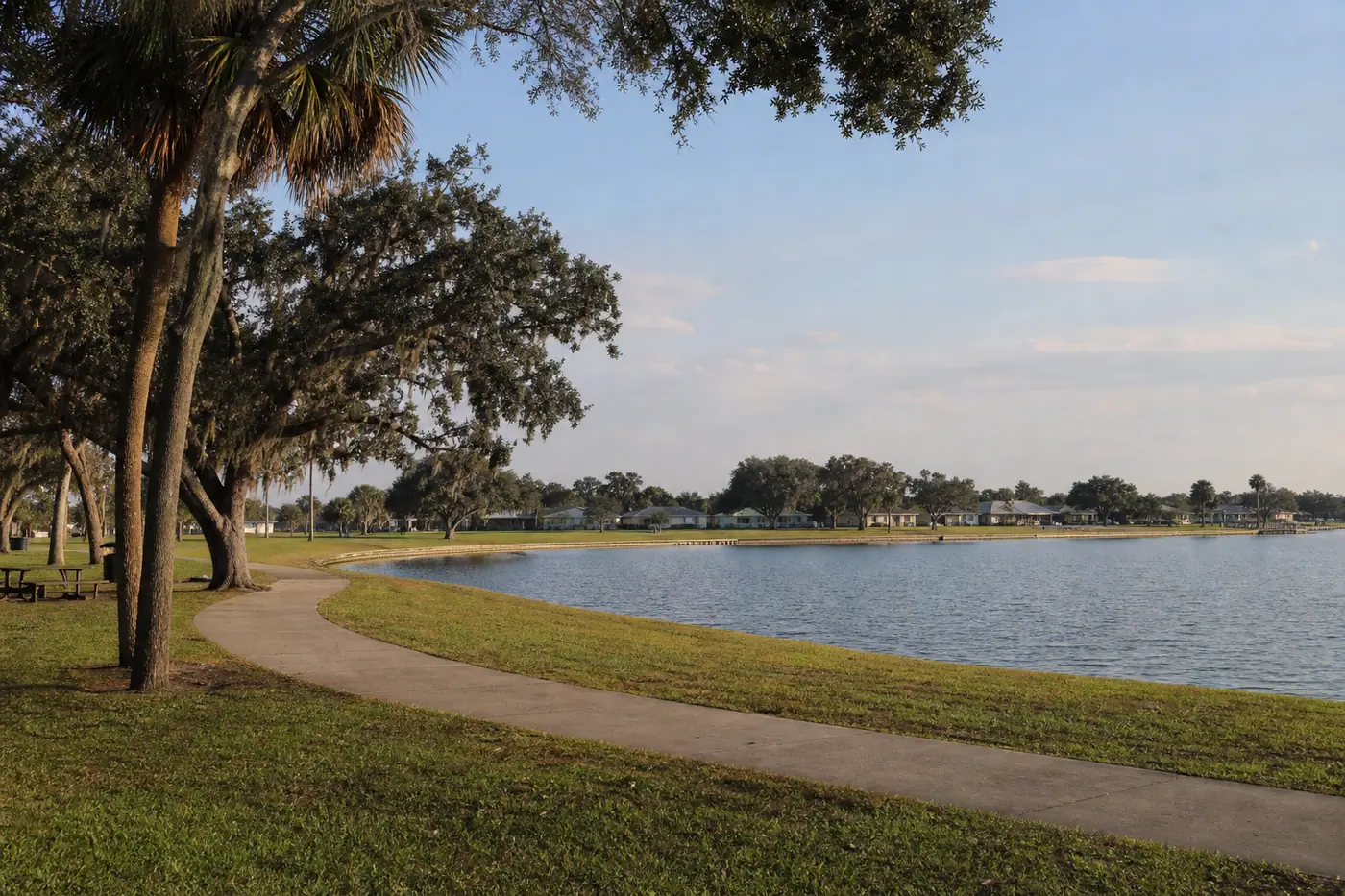 Auburndale lake park with a walking path, sabal palms, and homes across the water.